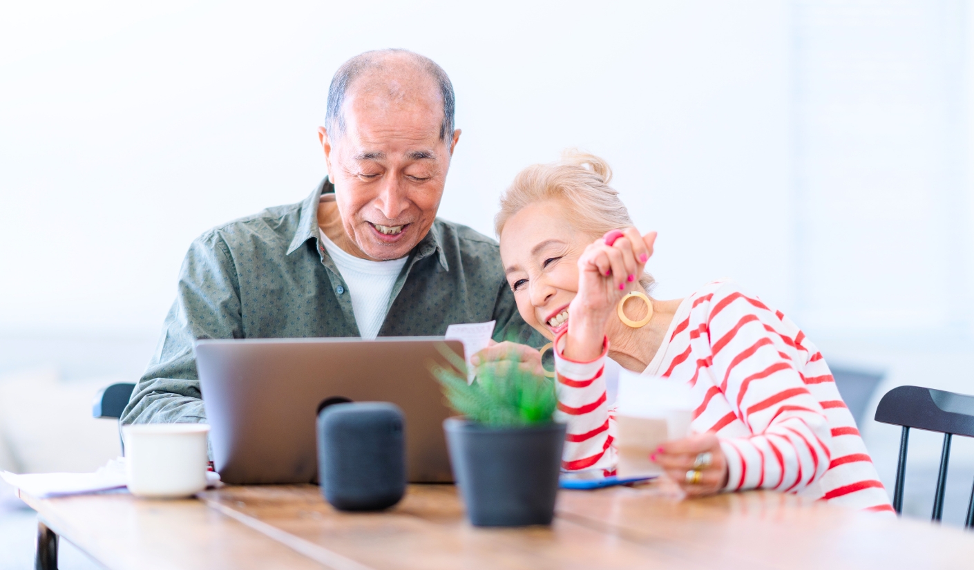 Smiling elderly couple sitting at a table, looking at a tablet together.
